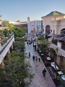 Modern shopping mall exterior with people walking and green landscaping.