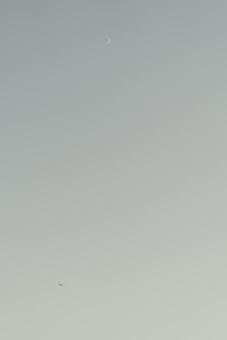 A serene sky with a crescent moon elegantly positioned near the top and a small airplane flying below, set against a gradient background transitioning from light green to pale blue.