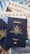 A blue Australian passport with gold embossing is placed on top of travel brochures and documents, featuring images of scenic locations and elements like blue skies and an envelope with red and blue stripes.