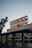 A well-lit neon sign for Landry's Seafood House is displayed on the roof of a building. The sign features bold red letters with a vintage look, and the facade below is adorned with stars. The surroundings include some trees and evening lighting, suggesting a relaxed outdoor atmosphere.