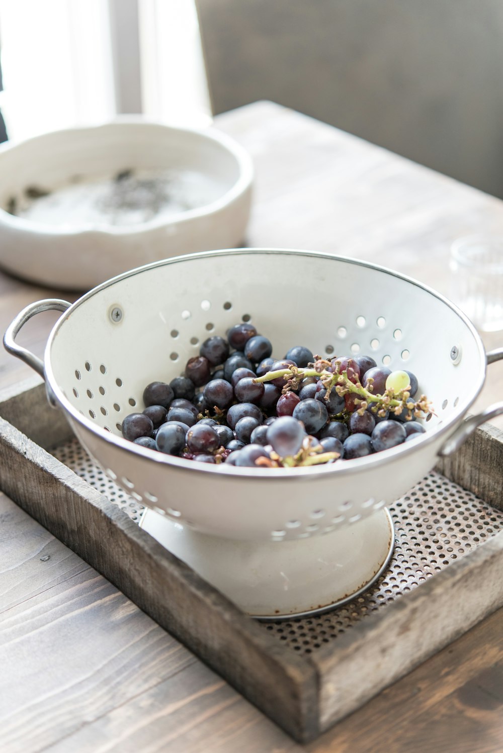 a white colander filled with grapes on top of a wooden tray