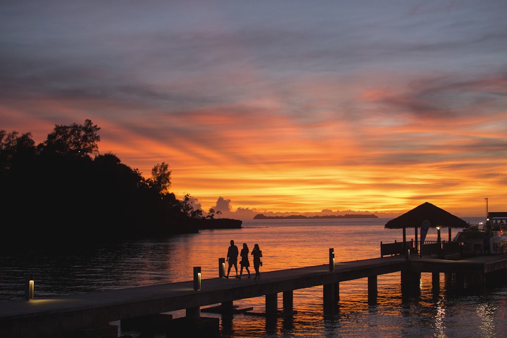a group of people standing on a dock at sunset