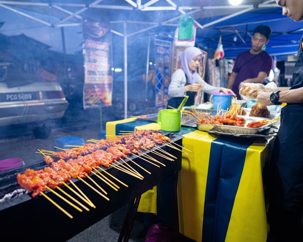 a group of people standing around a table with food on skewers
