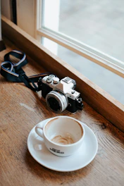 A candid shot of a vintage camera resting on a travel journal beside a steaming cup of coffee.