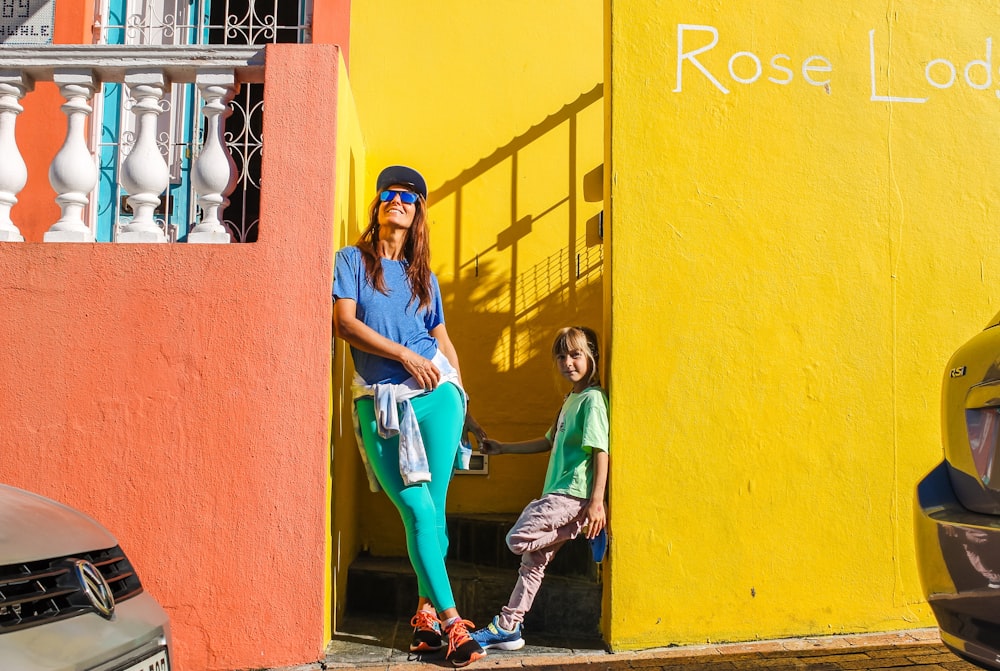 a woman standing next to a child in front of a yellow building