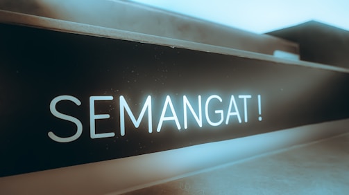 A close-up of a sign or board with the word 'SEMANGAT!' written in bold, bright letters, which appears to be illuminated or glowing against a dark background. The setting conveys a sense of motivation or encouragement.