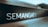 A close-up of a sign or board with the word 'SEMANGAT!' written in bold, bright letters, which appears to be illuminated or glowing against a dark background. The setting conveys a sense of motivation or encouragement.