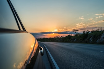 A vibrant car on a scenic road during sunset.