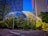 A modern urban landscape featuring two large geodesic dome structures surrounded by lush greenery. Tall office buildings with reflective glass facades rise in the background, and a streetlight is situated in the foreground. The sky is clear and blue, casting a vibrant light over the scene.