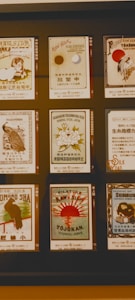 A display featuring nine vintage-style labels related to raw silk products from Japan, each designed with intricate illustrations and varied typography. The labels showcase different motifs, including birds, a lion, floral patterns, and traditional Japanese imagery, with a harmonious blend of colors and artistic styles.
