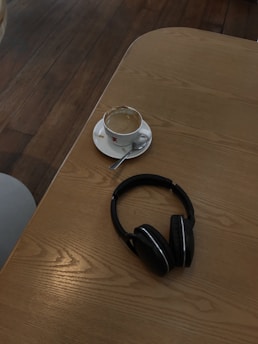 A cozy morning scene with a steaming cup of coffee beside headphones and a microphone on a wooden table.