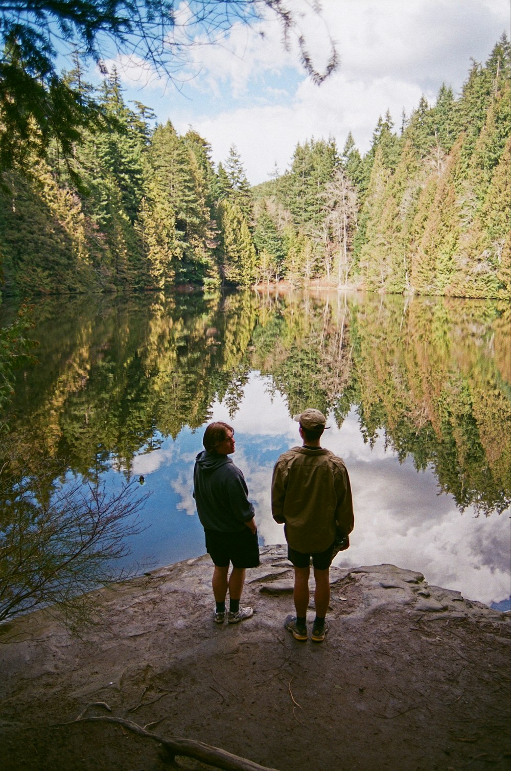 two people standing on a rock looking at a lake
