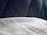 A close-up view of a textured gray fabric surface partially covered by a light, soft material. The background features a dark, patterned upholstery with diagonal stitching.