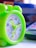 A small, vibrant green plastic clock with cartoon characters on its face. The clock features colorful numbers and yellow hands. It is placed next to a calculator on a white surface, with a blurred background showing blue and orange colors.
