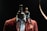 A mannequin adorned with a stylish brown blazer and shirt is topped with a wooden artist's mannequin sitting on its shoulder. The scene is set against a dark background, highlighting the contrast between the mannequin and its attire.