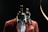 A mannequin adorned with a stylish brown blazer and shirt is topped with a wooden artist's mannequin sitting on its shoulder. The scene is set against a dark background, highlighting the contrast between the mannequin and its attire.