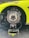A detailed view of a high-performance vehicle's wheel section without the tire, showcasing the complex brake disc and caliper system mounted on an advanced setup tool. The car's body is partially visible, painted in bright green with racing decals. The focus is on the meticulously detailed brake components and the equipment used for servicing or testing.