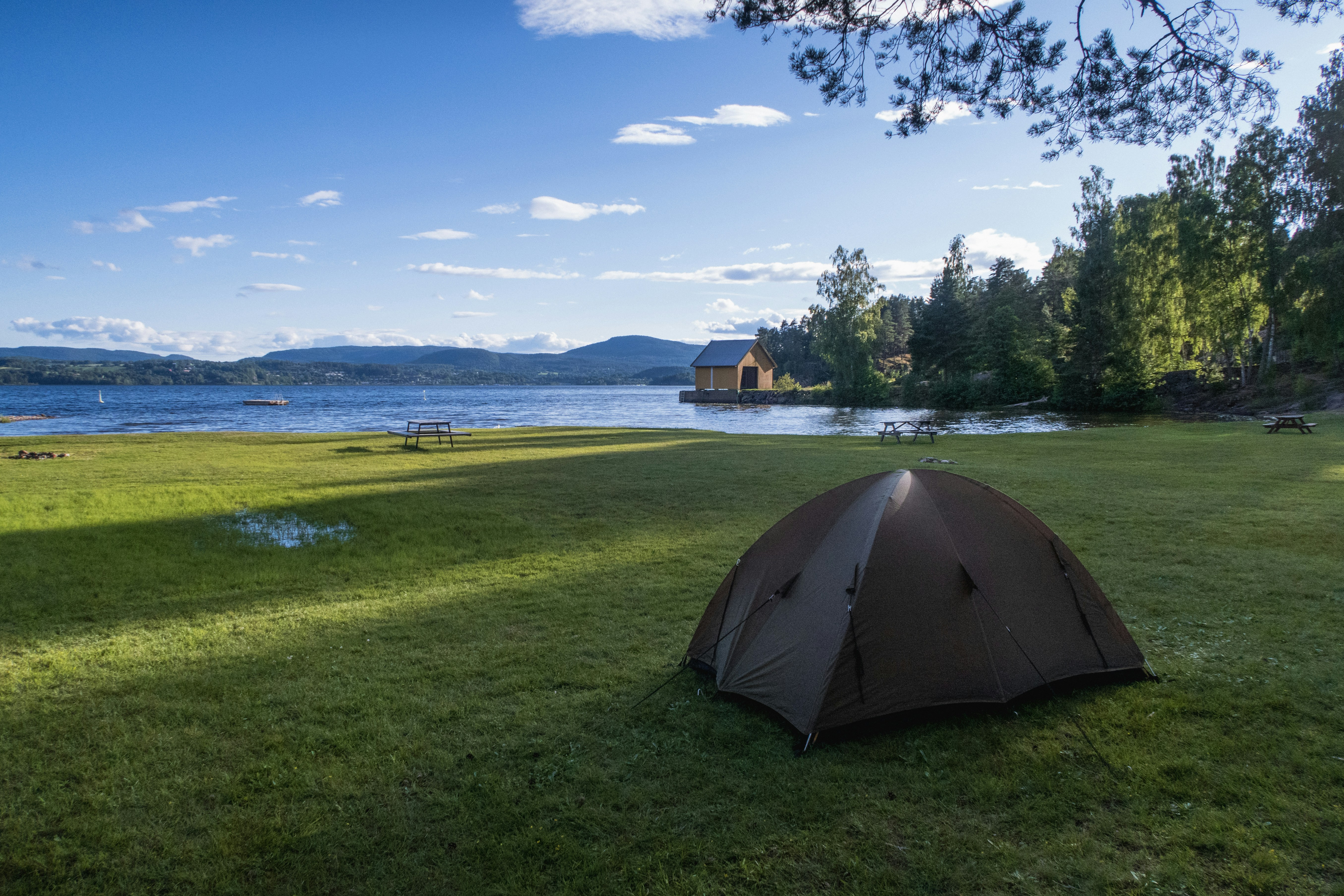 a tent pitched up on the grass near a lake