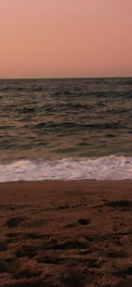 A serene beach scene with gentle waves lapping at the shore under a soft pink and orange sunset.