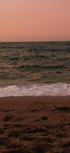 A serene beach view at sunset with soft waves lapping at the shore.