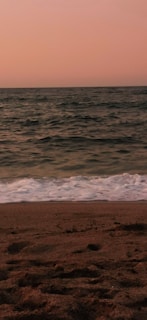 A serene beach at sunset with soft waves lapping at the shore.
