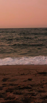 A serene beach scene with gentle waves lapping at the shore under a soft pink and orange sunset.