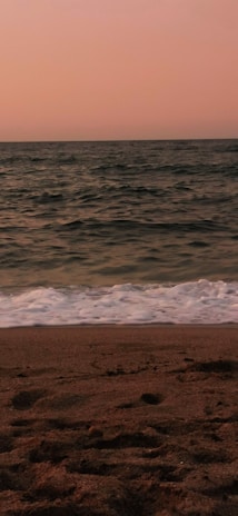A serene beach view at sunset with soft waves lapping at the shore.