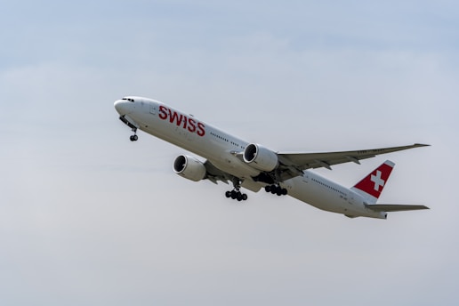 A Swiss Airlines jet is captured mid-flight, with its landing gear extended and prominent branding visible on the fuselage. The aircraft is set against a clear sky, suggesting a scene of aviation.