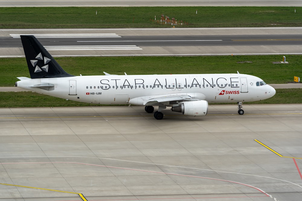 a white and black jet airliner on runway next to grass