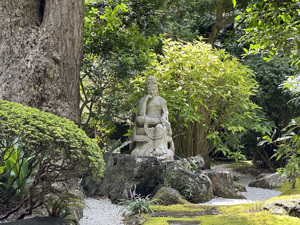 a statue of a buddha sitting on a rock in a garden