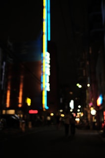 Soft-focus image of a city skyline at night with glowing neon signs in crimson and magenta.