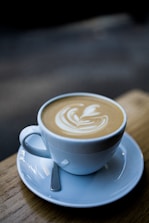 A close-up of a steaming latte with latte art in a ceramic cup on a wooden table.