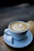 Close-up of a steaming latte with delicate latte art in a pastel ceramic cup on a wooden table.