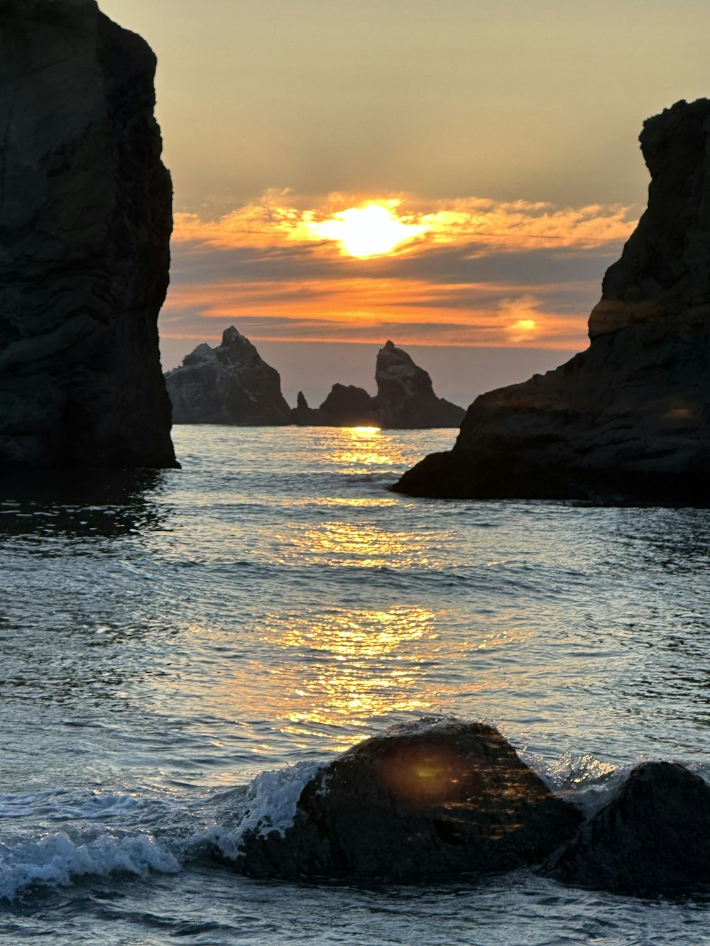 the sun is setting over the ocean with rocks in the foreground