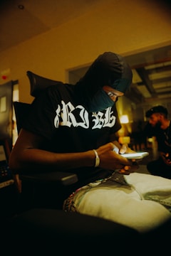 A shadowy figure typing on a smartphone in a dark room.