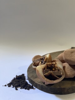 A close-up view of round, beige-colored confectioneries with a cross-section revealing chocolate chips and nuts inside. These treats are arranged on a rustic wooden board surrounded by a small heap of cocoa powder on a white surface.