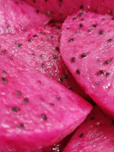 Close-up of a vibrant pink dragon fruit sliced open to reveal its speckled white flesh.