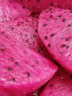 Close-up of vibrant, pink dragon fruit slices with black seeds scattered throughout the flesh, showing a textured and juicy surface.
