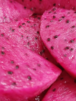 Close-up of vibrant, pink dragon fruit slices with black seeds scattered throughout the flesh, showing a textured and juicy surface.