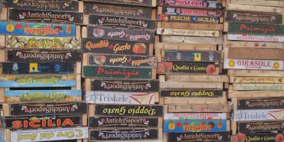 A stack of wooden crates with various Italian brand labels and colorful designs indicating different product origins and companies.