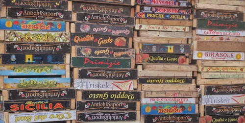 A stack of wooden crates with various Italian brand labels and colorful designs indicating different product origins and companies.