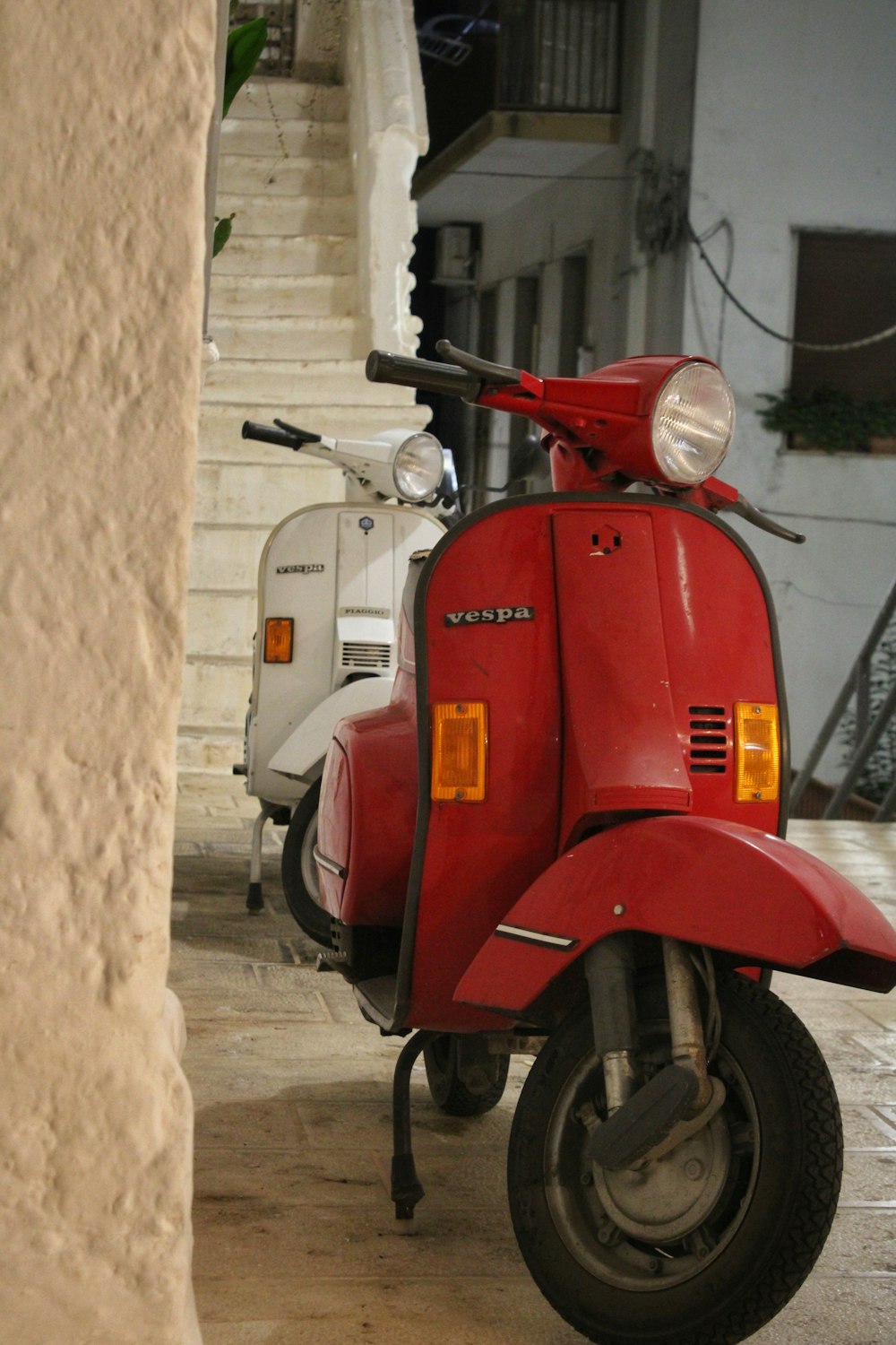 uma scooter vermelha estacionada ao lado de uma scooter branca