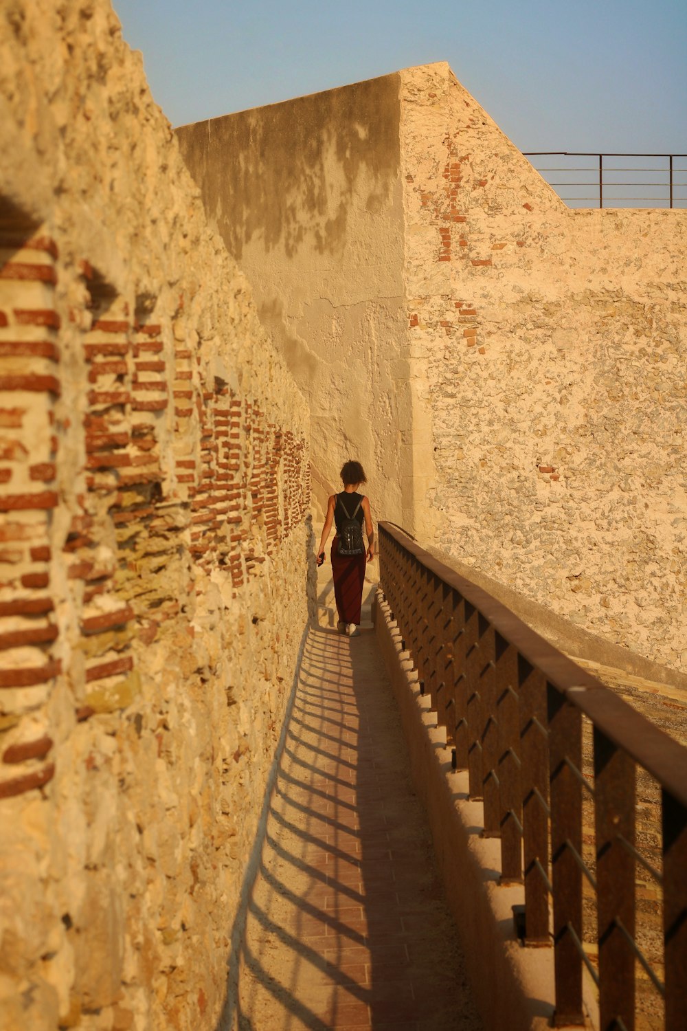 a woman walking down a walkway next to a stone wall