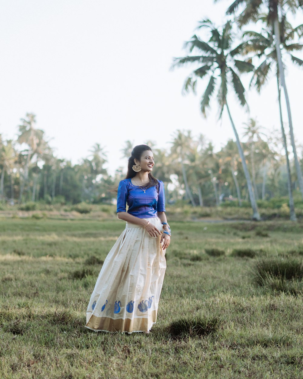 a woman standing in a field with palm trees in the background