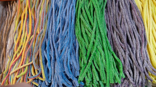 An assortment of colorful, sugar-coated candy strips is lined up in bundles. Each bundle consists of braids of different colors, including rainbow, blue, green, purple, and yellow.