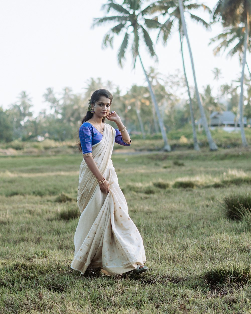a woman in a white and blue sari standing in a field