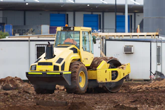 A bright yellow roll-off dumpster parked at a busy construction site with workers unloading debris.