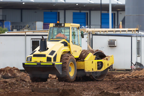 A bright yellow roll-off dumpster parked at a busy construction site with workers unloading debris.