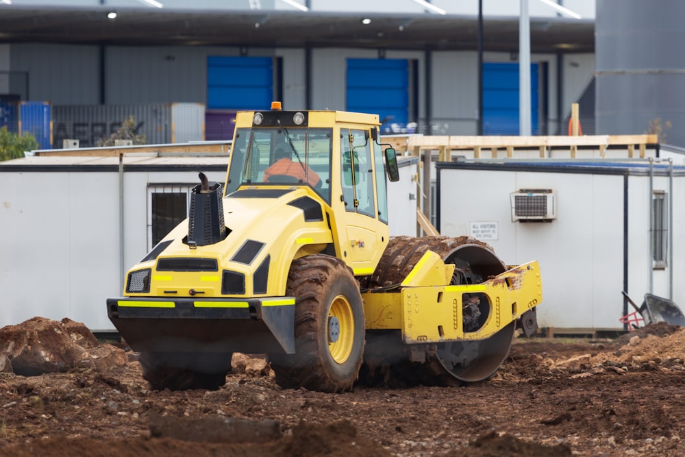 a yellow and black bulldozer digging dirt in front of a building