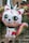 A colorful balloon shaped like a cute cat-unicorn hybrid, featuring large expressive eyes and a rainbow-colored mane and tail. The balloon is set against an outdoor background with blurred, natural elements.